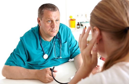 A young girl is complaining of headaches. A light medical study. The doctor of 45-50 years old in a green smock. Caucasian. Shallow depth of field. Focus is on the doctor. Shallow dof.