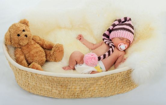 infant sleeping on a white sheepskin in a wicker basket.