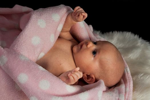 infant wrapped in a blanket on a black background.