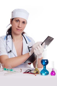 Scientist woman in lab coat with chemical glassware making notes, on white