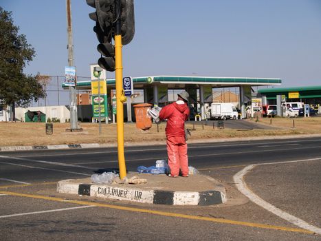 Man dressed in red stands on road island hailing traffic in his attempt to earn a living.