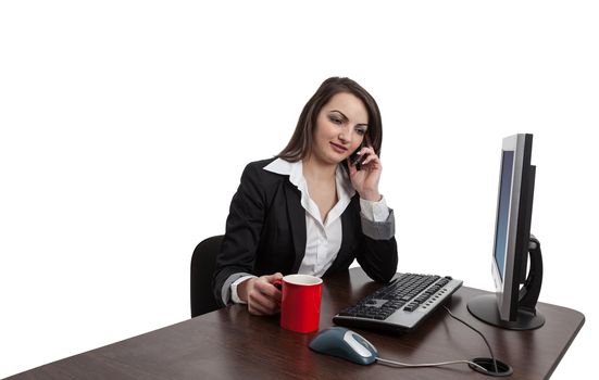 Portrait of a young brunette businesswoman with a red cup using a mobile phone at her desktop in an office.