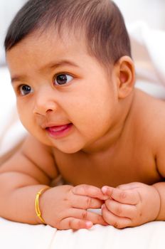 6 months old Indian baby girl smiling, lying on bed.