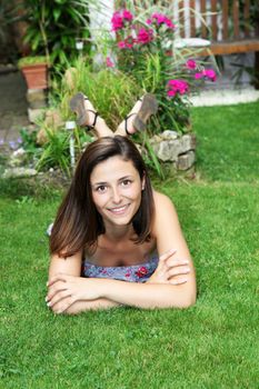 Attractive woman lying on her stomach relaxing on green grass with her feet in the air in the summer sunshine Attractive woman lying on her stomach relaxing on green grass with her feet in the air in the summer sunshine