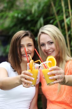 Two beautiful women raising their glasses and toasting with tropical orange cocktails while enjoying the sunshine on a summer vacation 