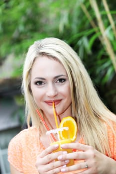 Beautiful smiling blonde woman drinking a healthy freshly squeezed orange cocktail on her tropical summer vacation 