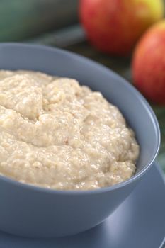 Bowl of cooked oatmeal porridge mixed with powdered maca or Peruvian ginseng (lat. Lepidium meyenii) with apples in the back (Selective Focus, Focus in the middle of the porridge) 