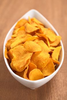 Crispy Peruvian sweet potato chips in white ceramic  bowl on wood (Selective Focus, Focus one third into the sweet potato chips)