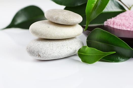 White zen stones, green leaves,  candle,  sea salt, white background.