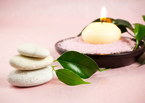 White zen stones, green leaves,  candle,  sea salt, pink background.