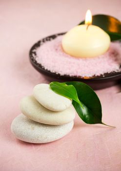 White zen stones, green leaves,  candle,  sea salt, pink background.