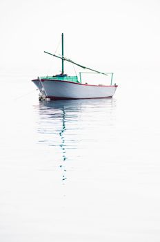 Lonely small fishing boat on very calm sea with smooth surface flowing together with sky