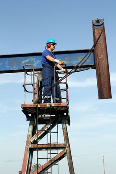oil worker in blue uniform standing at pump jack