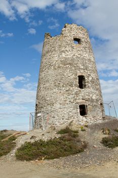 An historic stone built tower under renovation with a safety fence around against a blue sky with cloud.