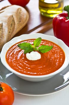 Tomato and pepper soup with cream and basil on top by a loaf of bread