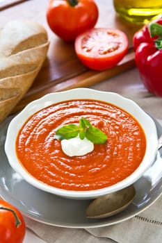 Tomato and pepper soup with cream and basil on top by a loaf of bread