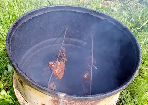 Ecologic fish smoke in smokehouse made of old rusty barrel.