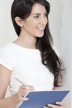 Young woman in white dress leaning against a white wall holding a blue folder