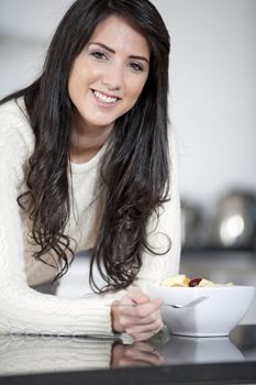 Young woman enyoying a bowl of fresh fruit in her kitchen