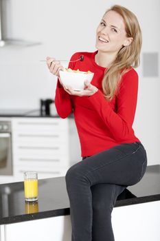 Young woman enjoying a bowl of fresh fruit in her kitchen with orange juice