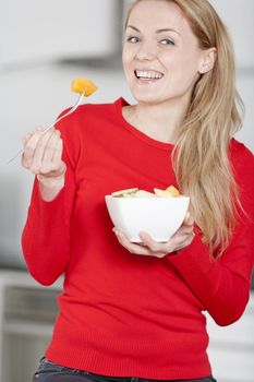 Young woman enjoying a bowl of fresh fruit in her kitchen