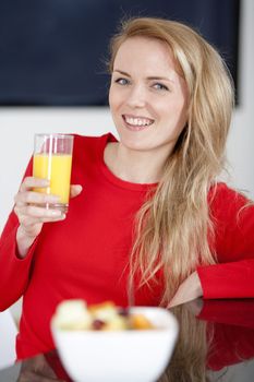 Young woman enjoying a bowl of fresh fruit in her kitchen with orange juice