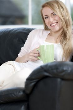 Young woman enjoying a hot drink at home on the sofa