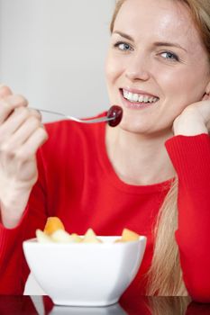 Young woman enjoying a bowl of fresh fruit in her kitchen