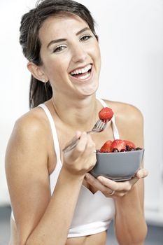 beautiful young woman in fitness clothes eating fresh fruit from a bowl at home