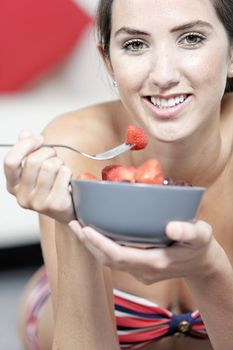 Beautiful young woman enjoying fresh fruit for breakfast in a red bikini