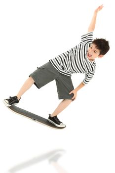 Attractive 8 year old boy playing on video game skateboard controller jumping over white background.