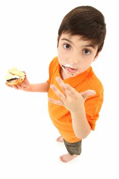 Attractive 8 year old boy standing with donut and cake licking food off fingers.