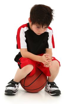 Sad elementary school boy sitting on basketball sad crying expression on face.