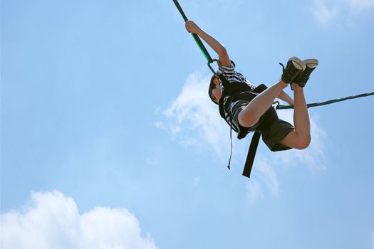 Happy 8 year old french-american boy bungee jumping against a blue and clouded sky with clipping path.