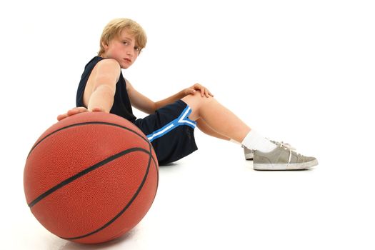 Young attractive teen boy child sitting with basketball in uniform over white serious expression. 