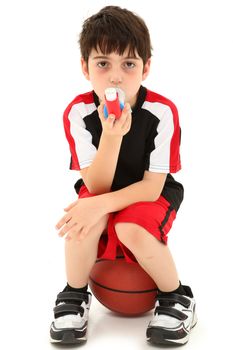 Boy Child with exercise or sport induced asthma attack sitting on basketball over white.