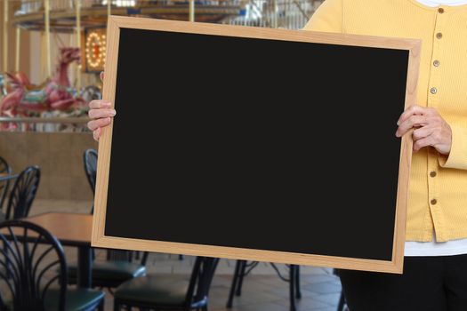 Woman holding blank chalkboard in front of carousel restaurant area.