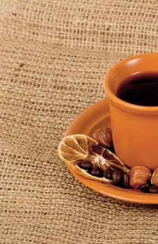 Closeup shot of freshly prepared cup of italian espresso with cinnamon, coffe beans, nuts and lemon over sacking