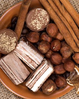 Sweets, cinnamon, nuts and coffee beans on a saucer, on burlap background.