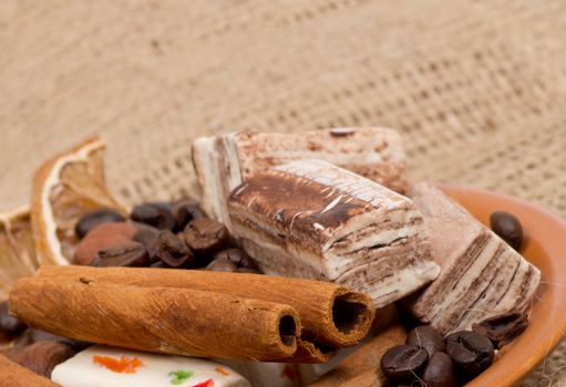 Sweets, cinnamon, nuts and coffee beans on a saucer, on burlap background.