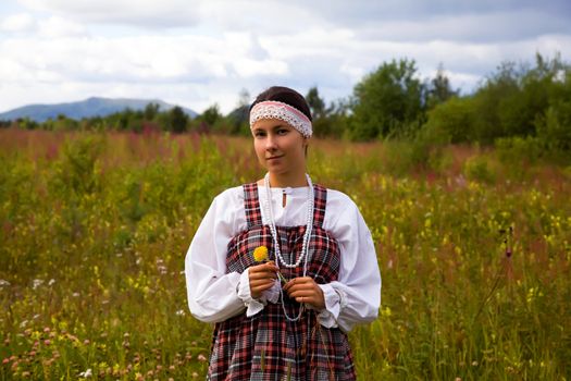 The girl in national dress on a background of flower meadow