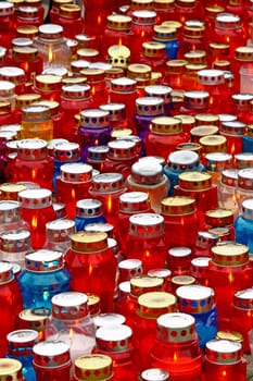 A lot of illuminated votive candles glows on a grawe, lantern