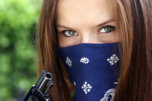 A woman holds a revolver with a bandanna over her face