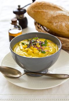 Corn soup with some fresh corn and sprout on top by a loaf of bread