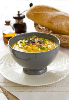 Corn soup with some fresh corn and sprout on top by a loaf of bread