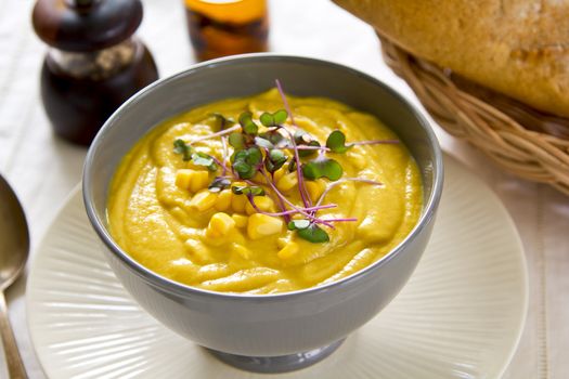 Corn soup with some fresh corn and sprout on top by a loaf of bread