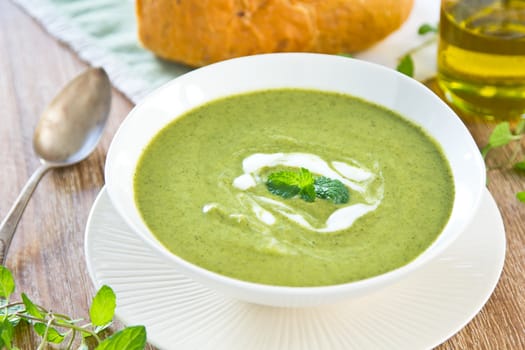 Pea,mint and celery soup with cream on top by a loaf of bread