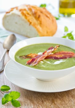 Pea,mint and celery soup with cream and bacon on top by a loaf of bread
