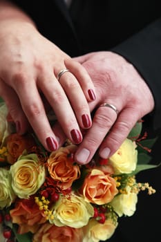 Hands of the groom and the bride on a wedding bouquet