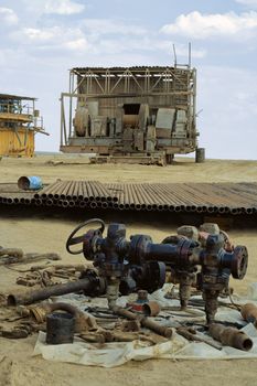 Old winch spread out on plastic sheeting on the desert sand with a drilling rig in the background